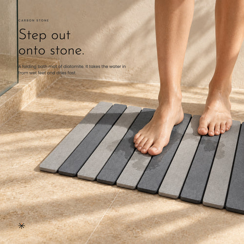 Bare feet stepping onto Carbon Stone outside a shower in soft sunlight